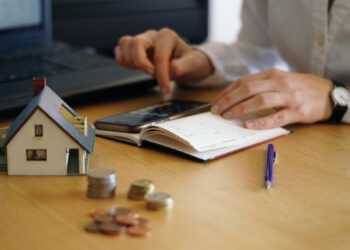 Profesional revisando proyecciones financieras y estrategias de inversión en un entorno equipado con modelos arquitectónicos, monedas representativas del capital y tecnología de punta. Esta escena refleja el análisis riguroso y la planificación estratégica indispensables para el éxito de proyectos inmobiliarios premium y desarrollos hoteleros exclusivos. Un enfoque orientado a maximizar el retorno sobre la inversión, asegurando oportunidades sólidas y rentables en el sector inmobiliario de alta gama.