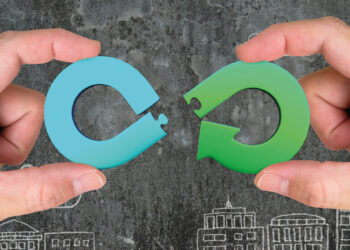 Dos manos sostienen piezas circulares de rompecabezas en azul y verde, diseñadas en forma de flechas que encajan perfectamente. El fondo oscuro, realzado por siluetas blancas de edificios, representa la innovadora iniciativa "Reciclar para Construir" de Saint-Gobain en Santa Catarina. Este proyecto integra sostenibilidad y vanguardia arquitectónica, ofreciendo desarrollos inmobiliarios premium que optimizan recursos y elevan los estándares medioambientales-una propuesta exclusiva para inversores y compradores que buscan excelencia, responsabilidad social y plusvalía en cada metro cuadrado.