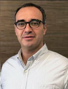 Un ejecutivo de perfil distinguido, con cabello oscuro y gafas, luce una camisa clara de corte impecable mientras se presenta frente a un elegante fondo en madera. Con una actitud segura y profesional, está listo para abordar los mitos más comunes del sector hipotecario en México, brindando claridad y orientación estratégica a inversionistas y compradores que buscan tomar decisiones informadas en el mercado inmobiliario premium.