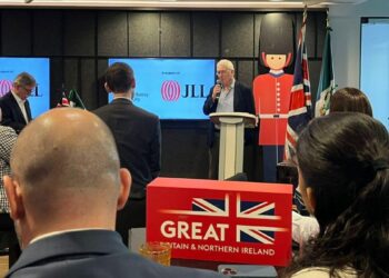 Un representante se dirige a un selecto grupo de asistentes en un auditorio exclusivo, respaldado por pantallas que exhiben la marca JLL y subrayan pilares clave: activos inmobiliarios de alto valor y sustentabilidad. El entorno está cuidadosamente ambientado con emblemas distintivos del Reino Unido, como la bandera británica y figuras icónicas, proyectando solidez internacional. En primer plano, una elegante caja con el logotipo GREAT BRITAIN & NORTHERN IRELAND refuerza el enfoque en oportunidades premium para inversores y compradores que buscan participar en los mercados inmobiliarios más dinámicos, sostenibles y prestigiosos a nivel global.