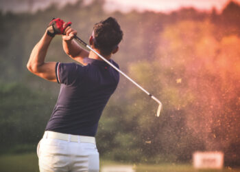 Un golfista, ataviado con camisa azul marino y pantalón blanco, ejecuta un elegante swing que levanta una estela de tierra, reflejando la sofisticación y el dinamismo del turismo de golf en México. Rodeado de verdes paisajes arbolados y luz natural cuidadosamente integrada al entorno, este escenario representa el atractivo exclusivo que buscan inversores y compradores exigentes: calidad de vida premium, contacto privilegiado con la naturaleza y acceso a experiencias deportivas de alto nivel en desarrollos inmobiliarios selectos.
