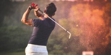 Un golfista, ataviado con camisa azul marino y pantalón blanco, ejecuta un elegante swing que levanta una estela de tierra, reflejando la sofisticación y el dinamismo del turismo de golf en México. Rodeado de verdes paisajes arbolados y luz natural cuidadosamente integrada al entorno, este escenario representa el atractivo exclusivo que buscan inversores y compradores exigentes: calidad de vida premium, contacto privilegiado con la naturaleza y acceso a experiencias deportivas de alto nivel en desarrollos inmobiliarios selectos.