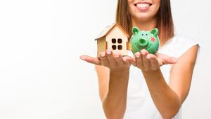 Una mujer sonriente, sobre un fondo blanco minimalista, sostiene en una mano una elegante casa de madera y en la otra una alcancía verde con diseño floral. Esta imagen representa el valor creciente de la vivienda premium en México proyectada para 2025, destacando la inversión inteligente y el atractivo potencial de apreciación que ofrece el sector inmobiliario exclusivo del país.