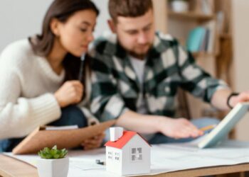 Una mujer y un hombre se reúnen en una mesa en México analizando cuidadosamente documentación relevante y notas estratégicas. Al frente, un modelo arquitectónico de vivienda premium y una planta ornamental destacan el enfoque de la conversación: la evaluación del valor inmobiliario y la revisión de documentos clave, posiblemente relacionados con INBAPREVI. Este escenario refleja el compromiso con procesos rigurosos de análisis para la adquisición o inversión en propiedades exclusivas, asegurando decisiones informadas dentro del sector inmobiliario de alto nivel.