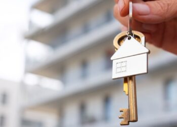 Una mano sostiene un llavero con un colgante en forma de casa y una llave, al frente de un exclusivo edificio residencial de fondo difuminado. Esta imagen simboliza el acceso a propiedades premium en desarrollos de usos mixtos modernos en Puebla, ofreciendo oportunidades excepcionales para inversores y compradores que buscan plusvalía, exclusividad y estilo de vida sofisticado.