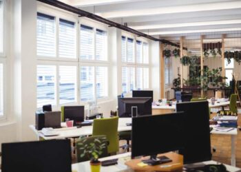 Oficina de diseño abierto con múltiples estaciones de trabajo, monitores de alta gama, sillas ergonómicas y detalles cuidadosamente seleccionados. Amplios ventanales permiten la entrada abundante de luz natural, generando un ambiente luminoso y atractivo. La presencia estratégica de plantas integradas al mobiliario acentúa el enfoque en el bienestar, tendencia clave en los desarrollos corporativos premium. Estas características distinguen las oficinas modernas en Querétaro ofrecidas por Solili, consolidándose como una opción preferente para inversionistas y compradores que buscan espacios exclusivos adaptados a las demandas actuales del mercado inmobiliario empresarial.