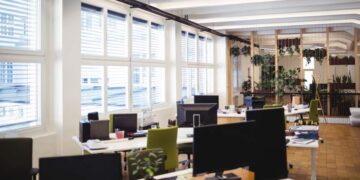 Oficina de diseño abierto con múltiples estaciones de trabajo, monitores de alta gama, sillas ergonómicas y detalles cuidadosamente seleccionados. Amplios ventanales permiten la entrada abundante de luz natural, generando un ambiente luminoso y atractivo. La presencia estratégica de plantas integradas al mobiliario acentúa el enfoque en el bienestar, tendencia clave en los desarrollos corporativos premium. Estas características distinguen las oficinas modernas en Querétaro ofrecidas por Solili, consolidándose como una opción preferente para inversionistas y compradores que buscan espacios exclusivos adaptados a las demandas actuales del mercado inmobiliario empresarial.