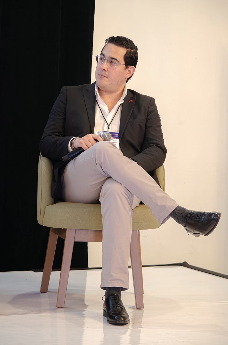 Un distinguido profesional, ataviado con un blazer negro, camisa blanca y pantalón claro, ocupa una elegante butaca verde oliva mientras interviene en un foro especializado sobre turismo de alto nivel en Puebla. Con una actitud reflexiva y mirada aguda tras sus gafas, sostiene el micrófono con confianza. Su presencia destaca en un entorno sobrio y minimalista que refleja sofisticación y enfoque; el escenario ideal para analizar las tendencias del turismo premium y su impacto directo en las oportunidades inmobiliarias exclusivas de la región -un atractivo clave para inversores o compradores que buscan activos diferenciados con alto potencial de valor.